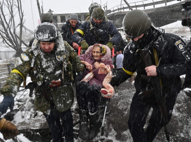 Ukrainian soldiers help an elderly woman cross a destroyed bridge during the evacuation of the city of Irbin, northwest of Kyiv, on March 8, 2022.