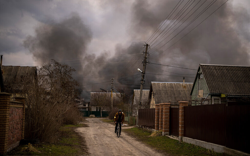 A Ukrainian man rides his bicycle near a factory and a store burning after it was bombarded in Irpin, on the outskirts of Kyiv, Ukraine, March 6, 2022. (AP Photo/Emilio Morenatti)