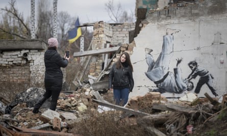 A woman takes a picture of another woman posing in front of a Banksy mural